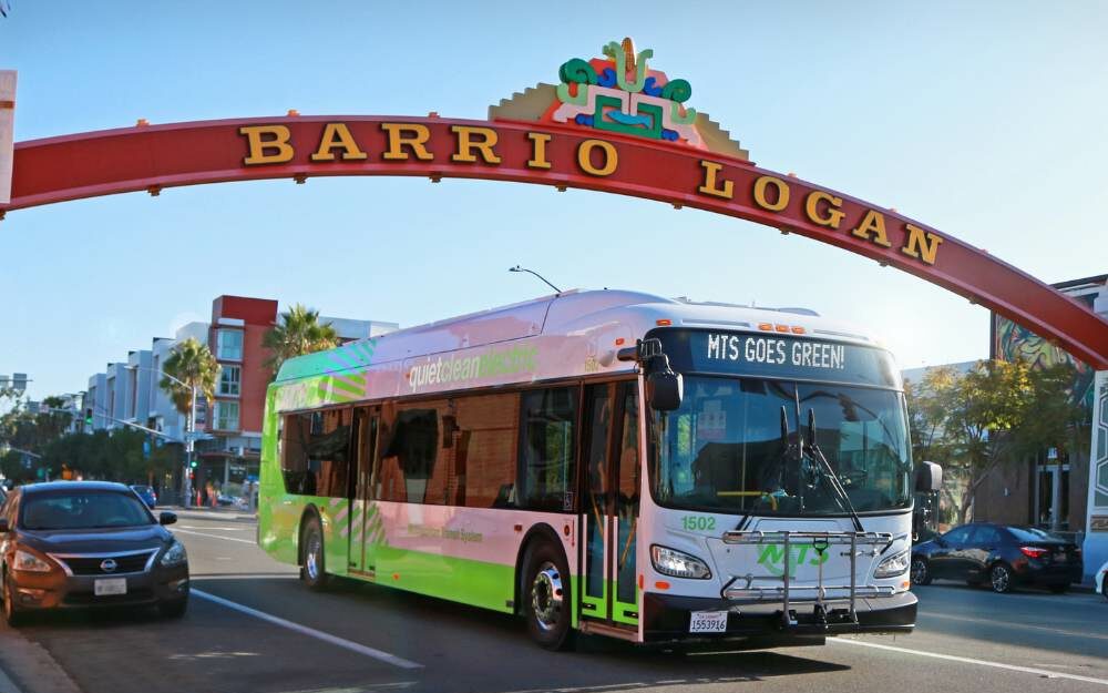 EV bus driving under Barrio Logan sign.